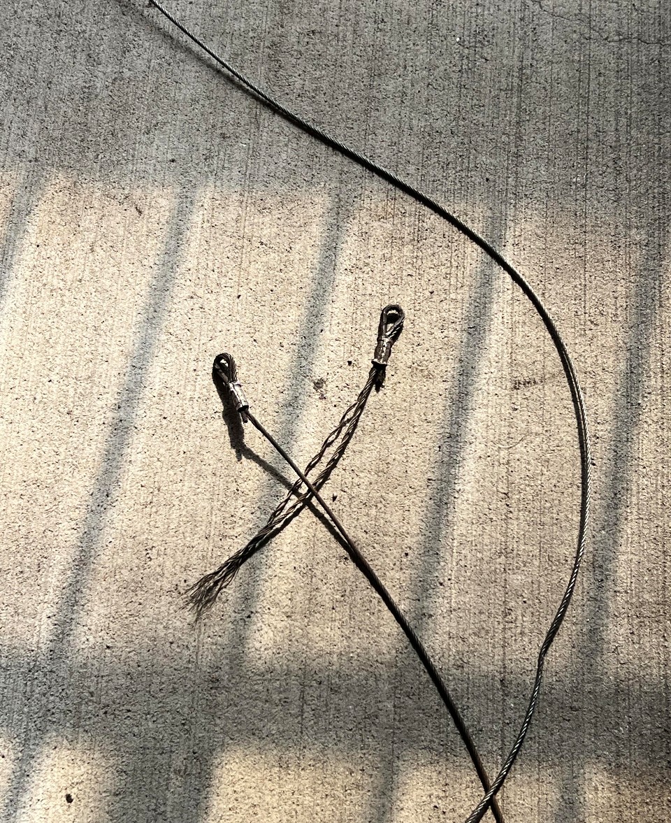 Frayed black cable with loops lies on a sunlit concrete surface, casting linear shadows.