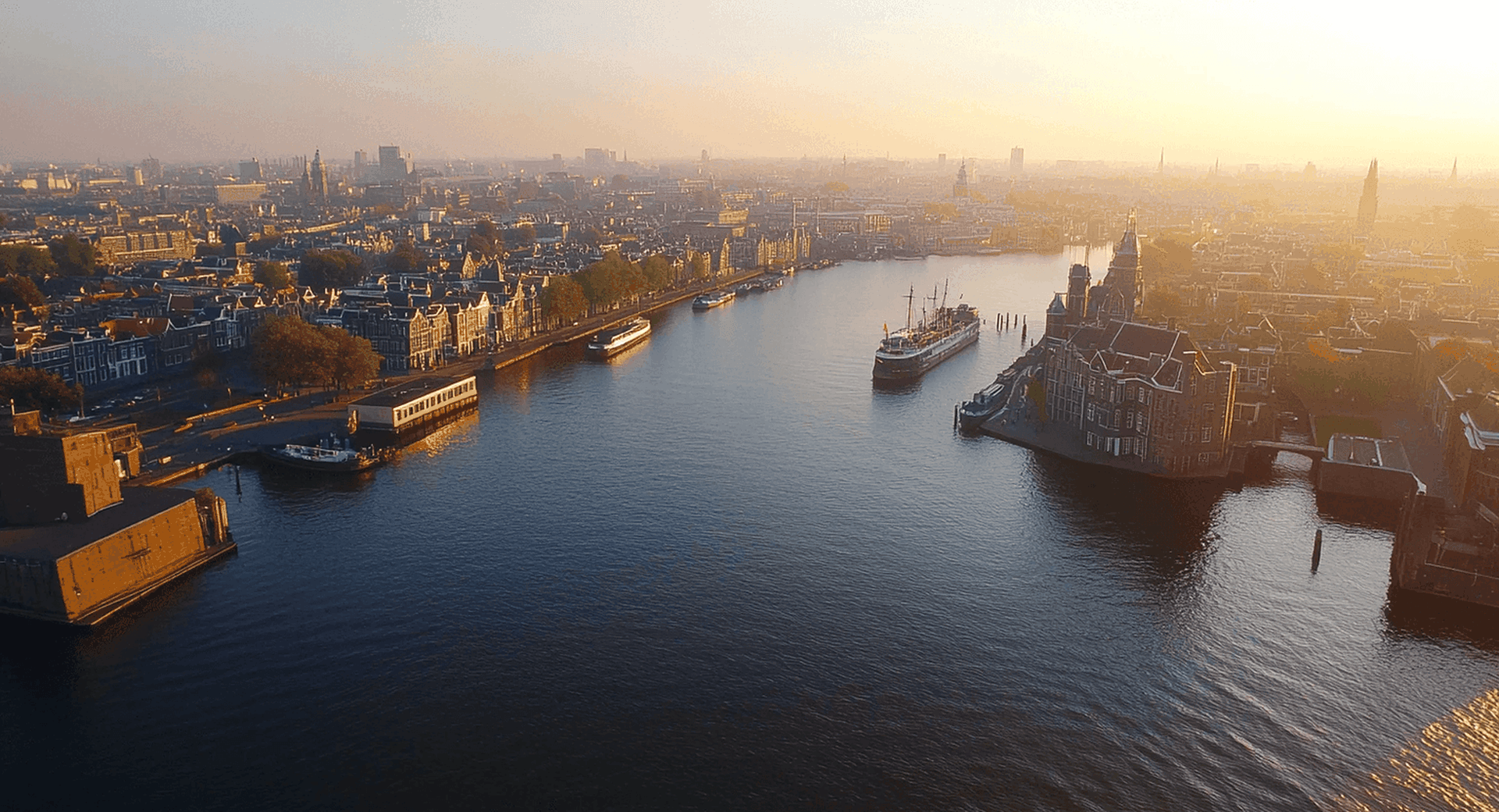 Luchtfoto van de grachten van Amsterdam bij zonsopgang met historische panden en boten op het water.