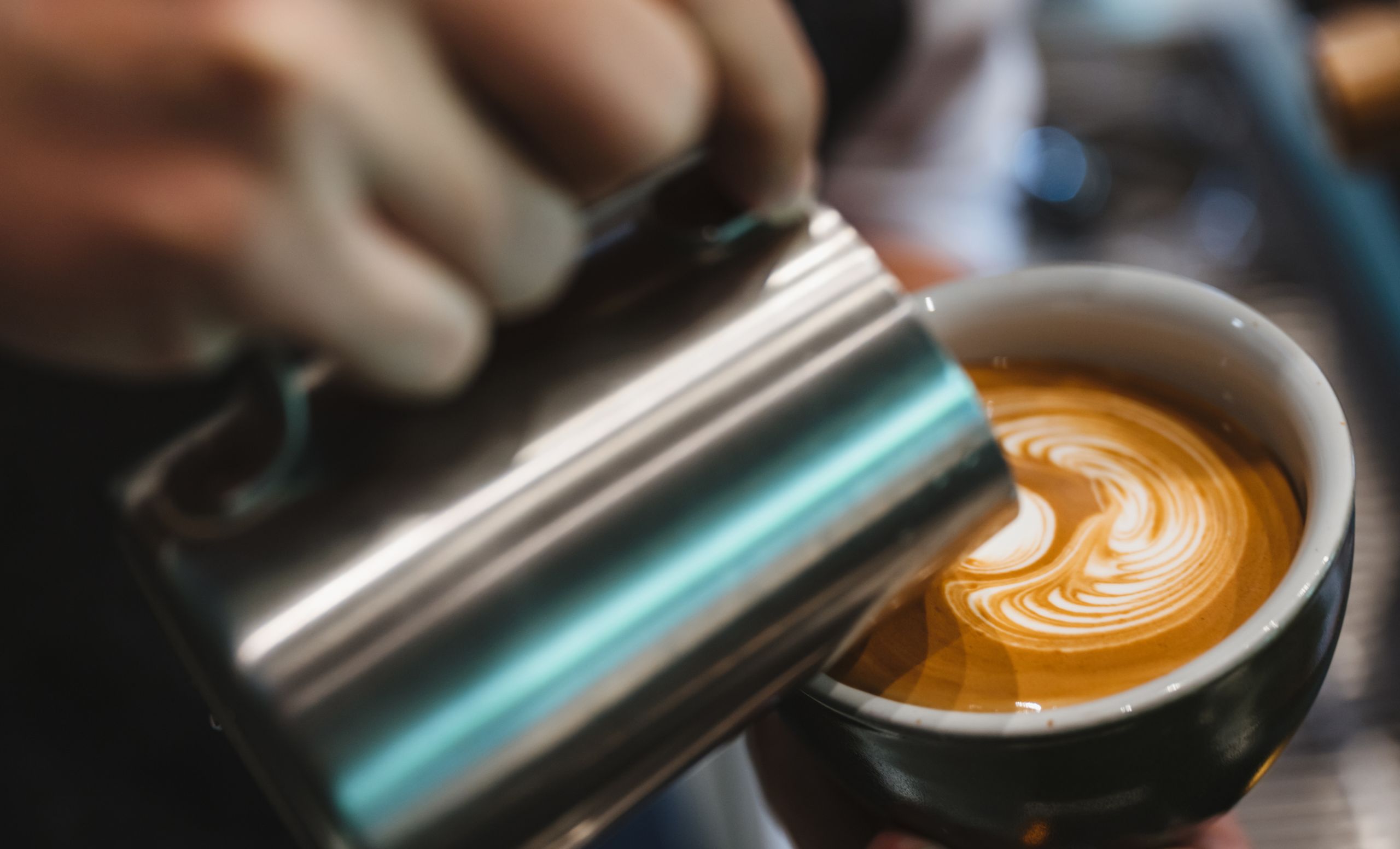 Närbild på en kopp där mjölk hälls i ett kreativt mönster.