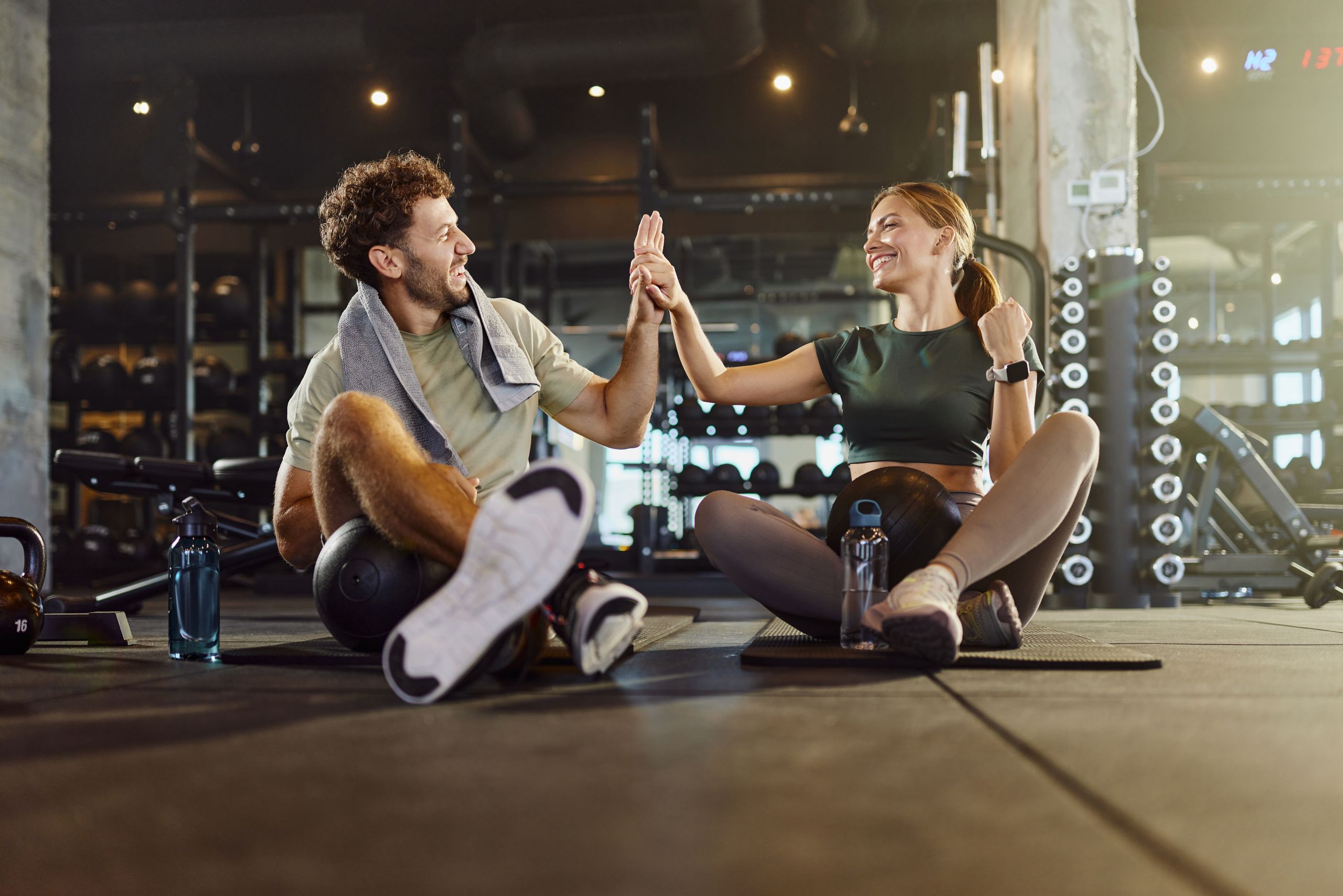 En man och en kvinna sitter på ett gym och ger varandra en high five.