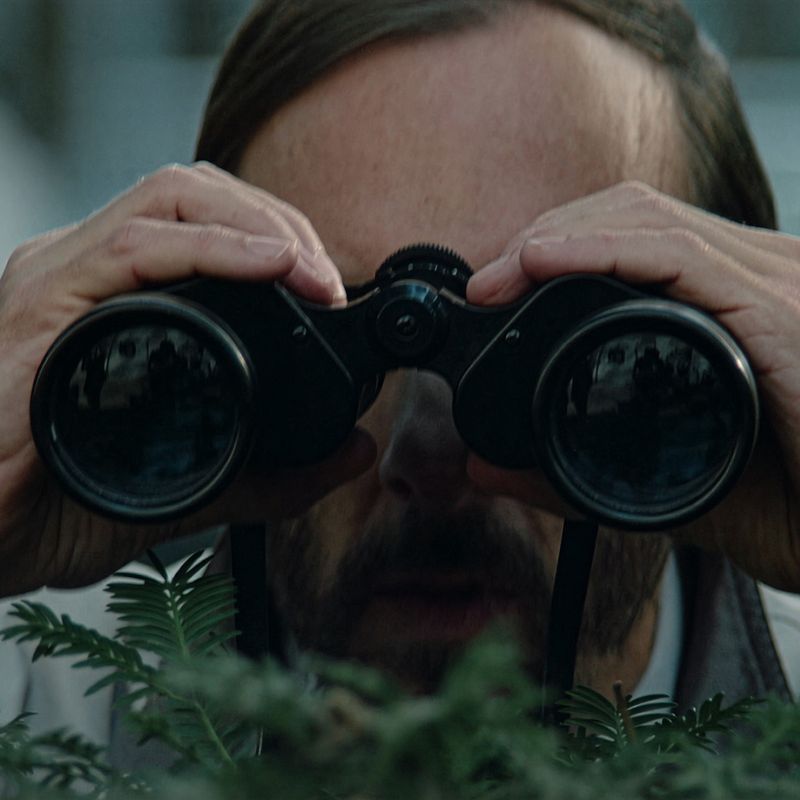 Nahaufnahme eines Manns der durch ein schwarzes Fernglas schaut