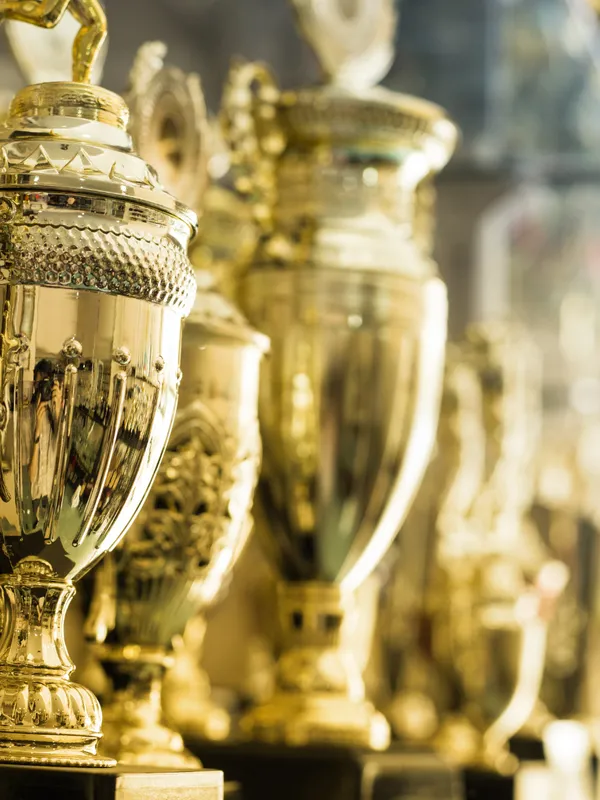 A close-up view of a row of golden trophies lined up on a shelf, glistening under bright light, symbolizing achievement and recognition.
