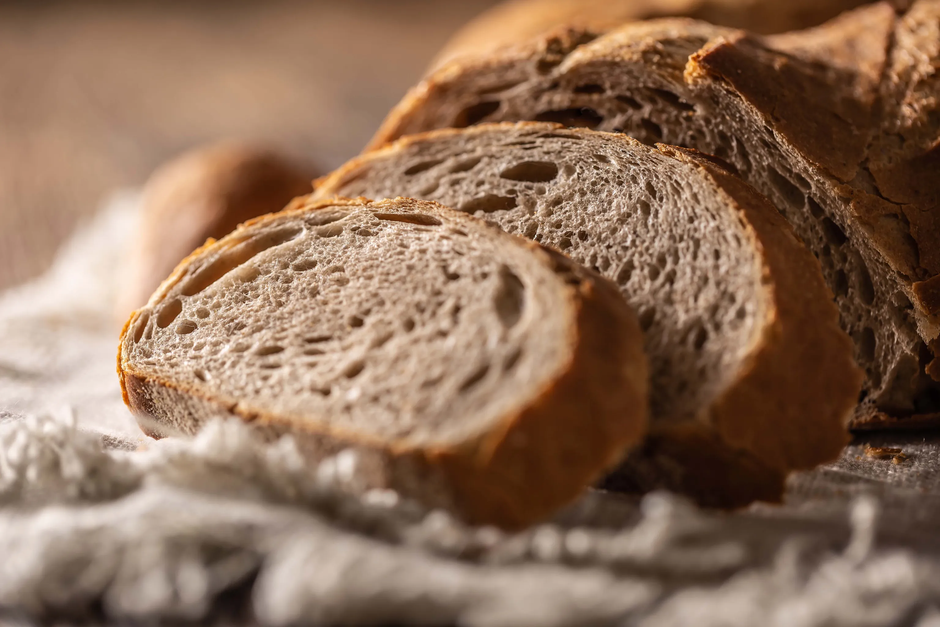 Nahaufnahme von geschnittenem Brot mit goldbrauner Kruste und luftiger Konsistenz auf einer Holzunterlage.
