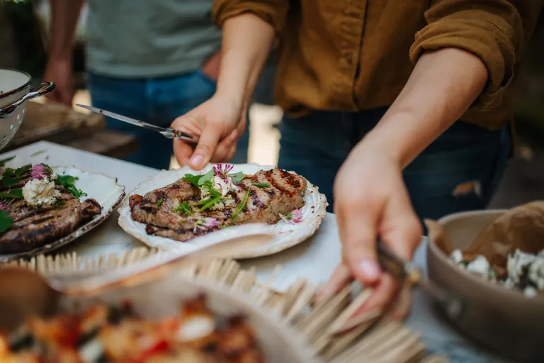 Person serviert frisch gegrilltes Steak mit Kräuterbutter und essbaren Blüten bei einer Grilljause