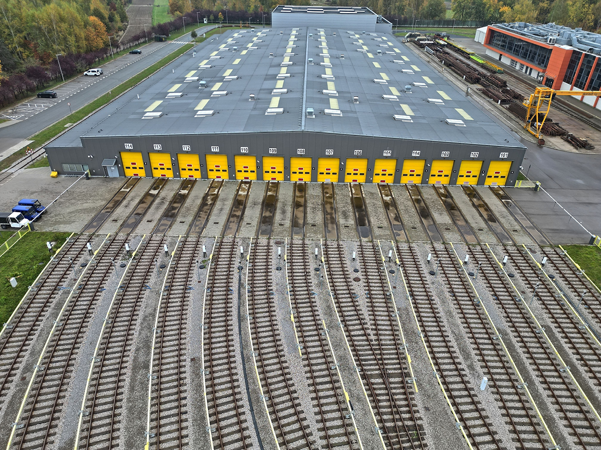 Aerial view of parallel railway tracks leading to a large depot building with numbered yellow doors.