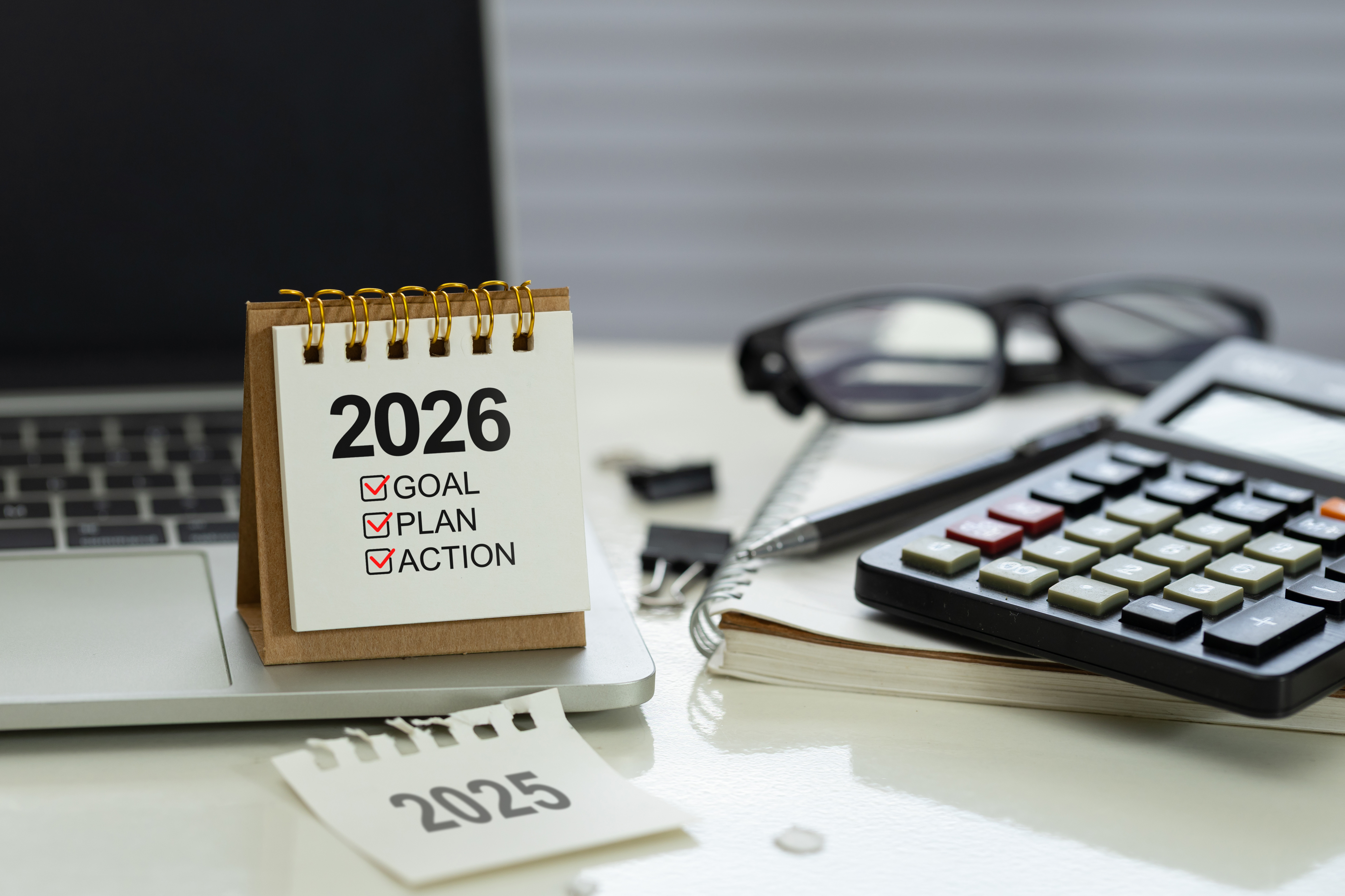 Kalender op bureau toont “2026: Doel, Plan, Actie” met een laptop, rekenmachine, bril en notitieboekje, symbolisch voor planning en productiviteit.