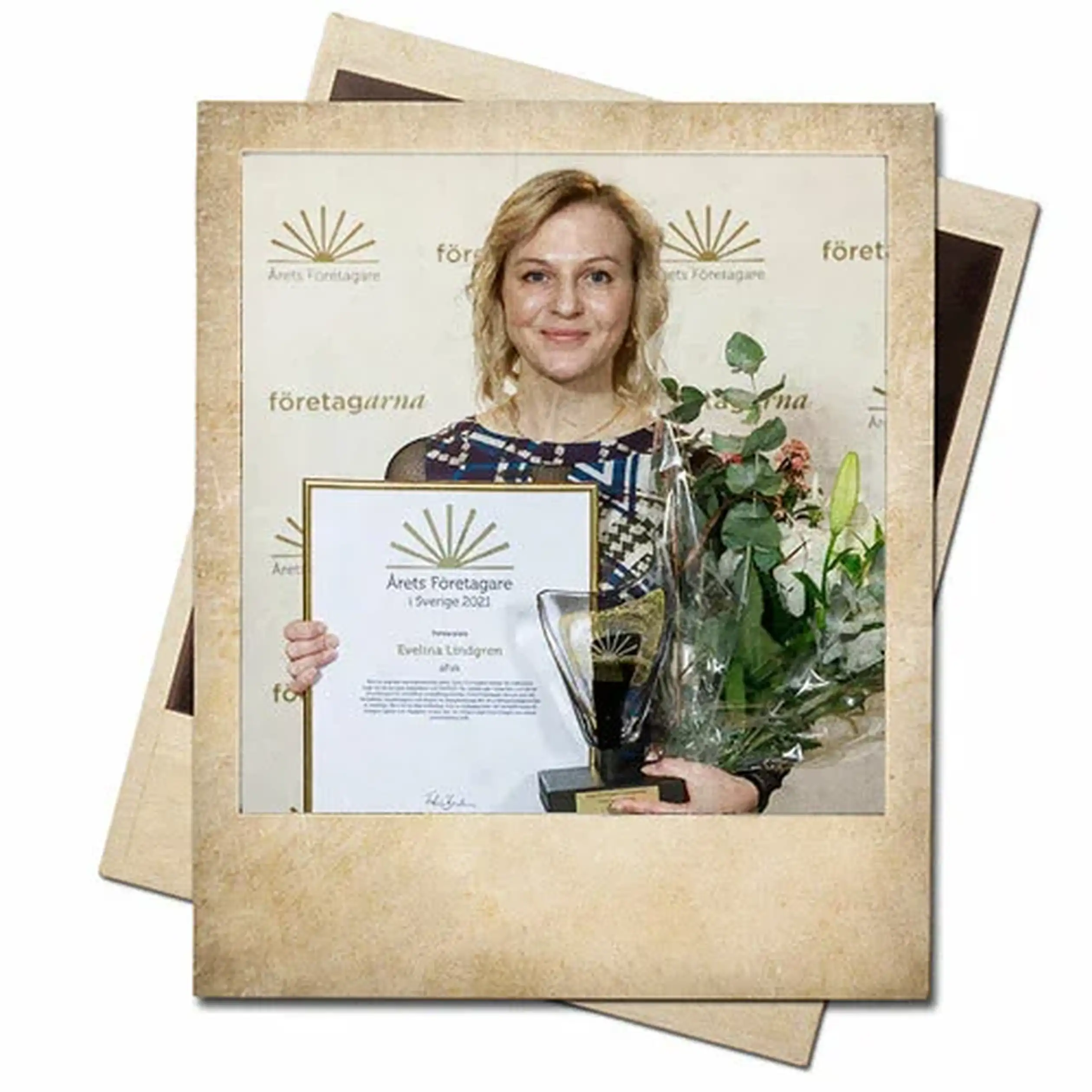 Woman holding a framed certificate and a trophy, standing against a patterned backdrop, also holding a bouquet of flowers.