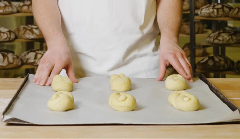 Mehrere fertig geformte Bäckerstriezel aus Germteig auf einem Backblech bereit zum Backen