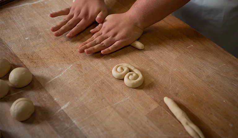 Eine Bäckerein beim Ausrollen und Formen von einzelnen Germteig-Teilen zu einem Schmetterling