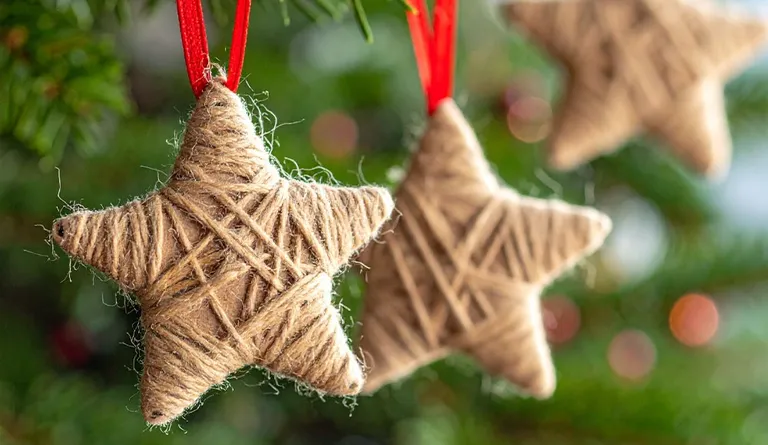 Sterne aus Karton umwickelt mit Juteband händen an roter Schleife im Christbaum