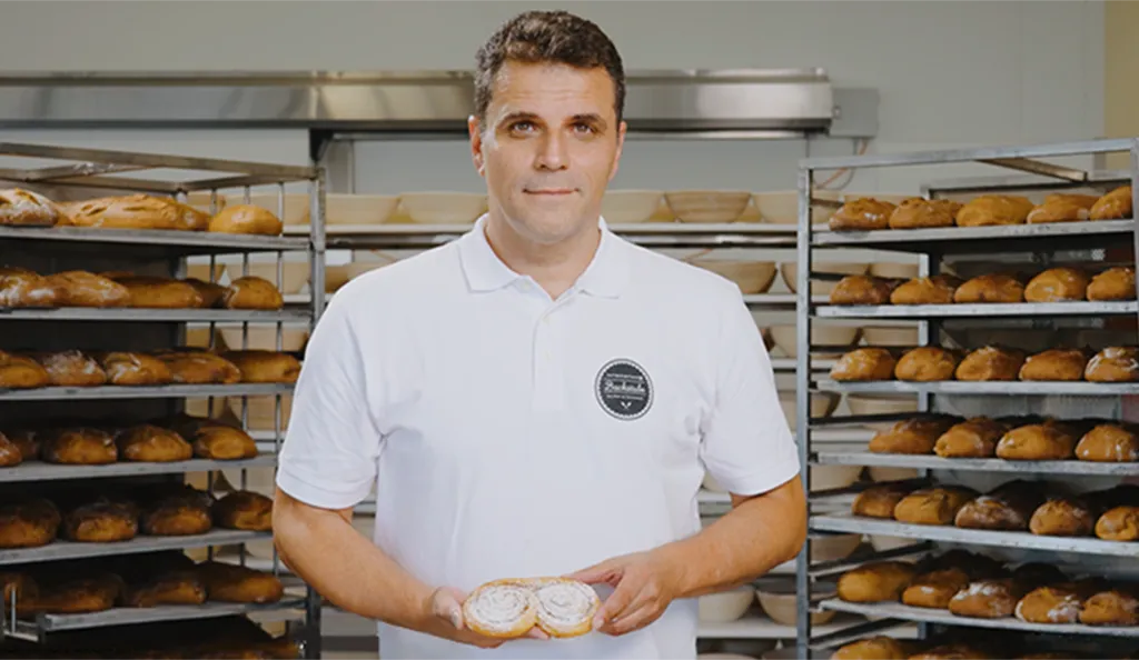 Bäckermeister Alexander Moucka der INTERSPAR-Bäckerei lächelt mit seinem Bäckerliebling in die Kamera