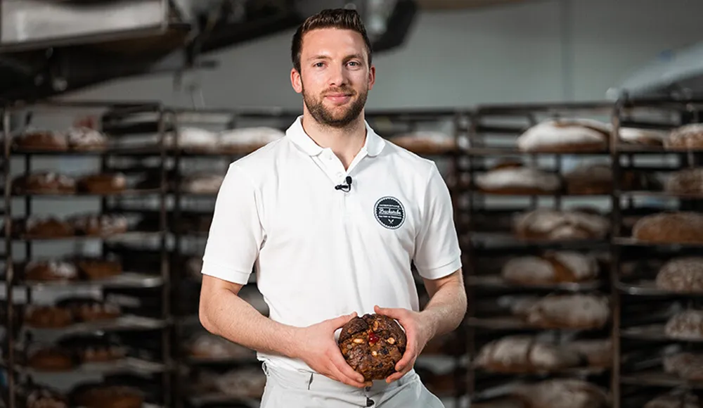 Handwerksbäcker Patrick Beschta der INTERSPAR-Bäckerei lächelt mit seinem Bäckerliebling in die Kamera