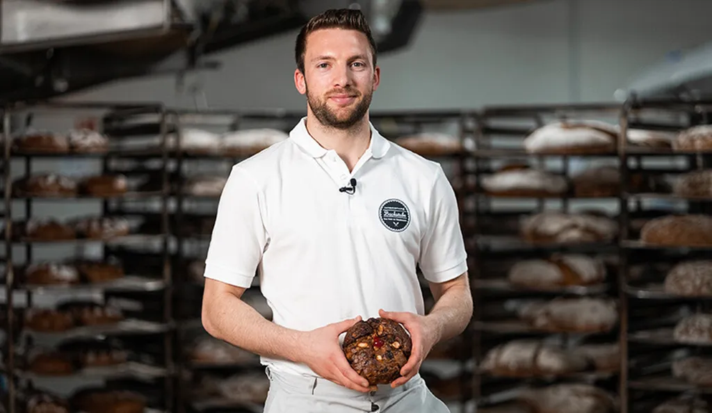Handwerksbäcker Patrick Beschta der INTERSPAR-Bäckerei lächelt mit seinem Bäckerliebling in die Kamera