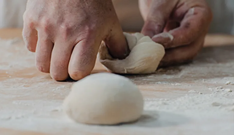 Frisch portionierte Handsemmel-Teiglinge werden von einem Bäcker zu Handsemmeln geschlagen