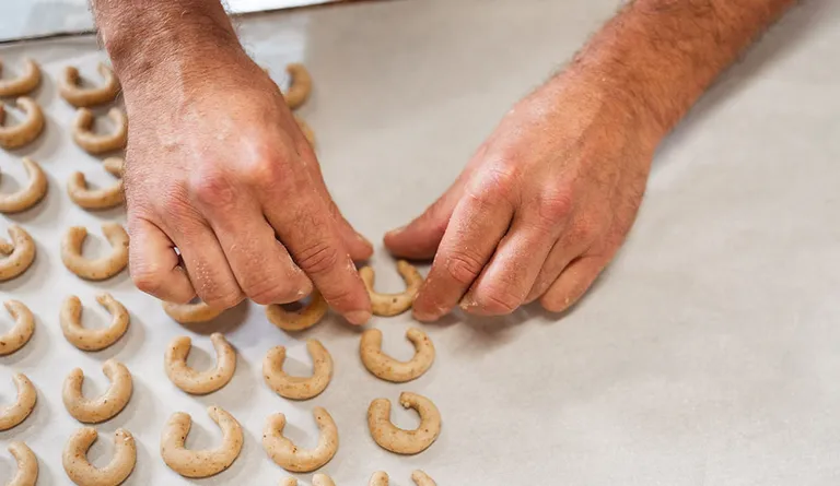 Ein Bäcker beim Formen einzener Vanillekipferl auf einem großen Backblech