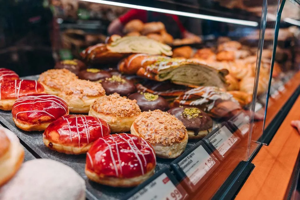 Eine Bäckereivitrine mit einer Auswahl an Faschingskrapfen, unter einer Glasabdeckung mit Preisschildern.