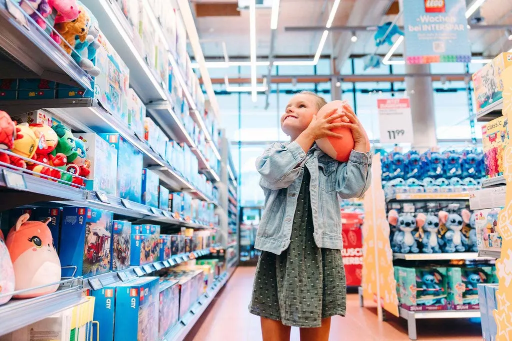 Ein kleines Mädchen mit einem Spielzeug in den Armen in der Spielsachen-Abteilung im INTERSPAR-Hypermarkt Hallein