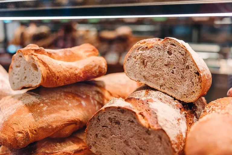 In einer Bäckerei sind verschiedene frisch gebackene Brote ausgestellt, die sich durch eine knusprige, braune Kruste und eine luftige Krume auszeichnen.