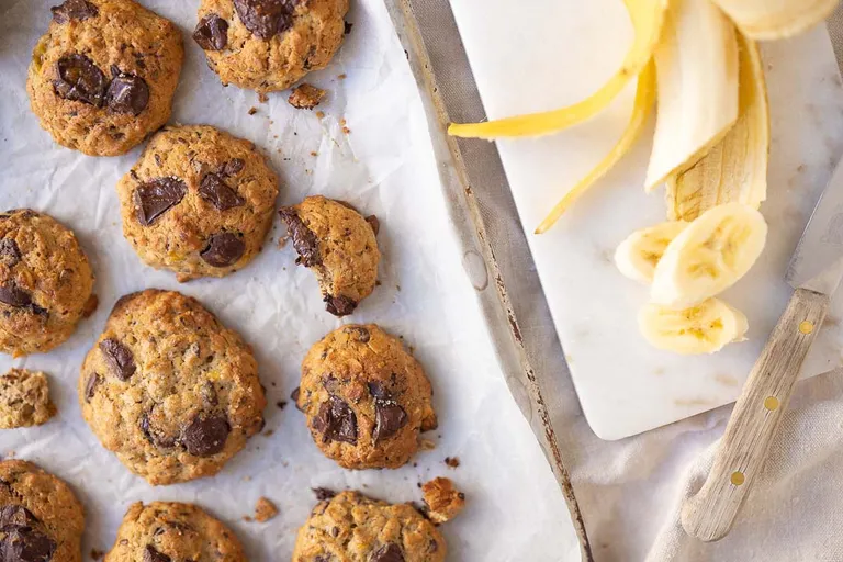 Ein Blech mit frischen Bananen-Hafer-Cookies neben einer in Stücke geschnitten Banane