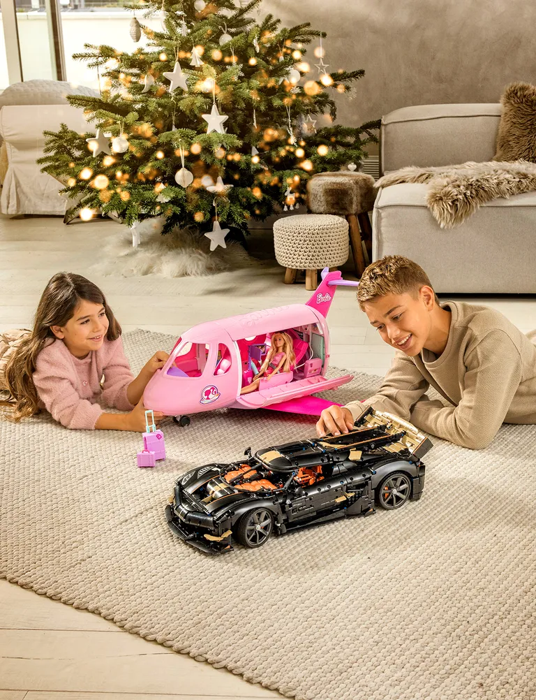 Zwei Kinder beim Spielen mit Spielsachen auf einem Teppich vor einem Weihnachtsbaum
