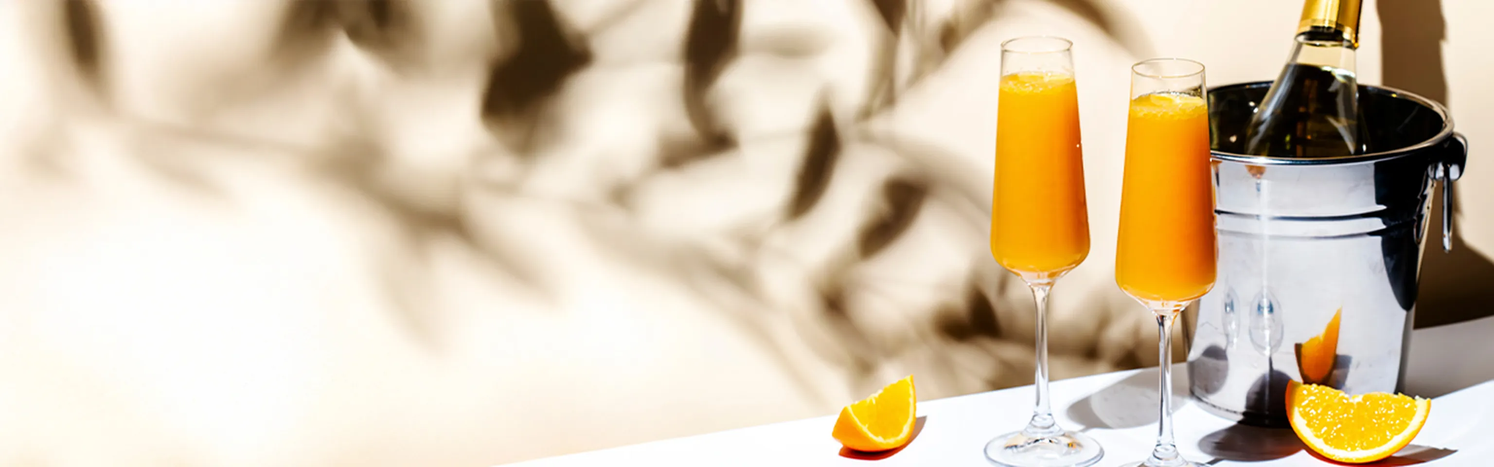 Zwei Mimosa-Cocktails mit Orangensaft und Schaumwein neben Orangenspalten und einer gekühlten Flasche