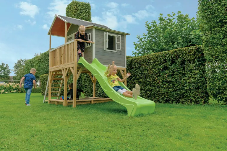 Kinder spielen mit einem Gartenspielhaus mit Sandkiste und Rutsche, im Garten mit klarem Himmel