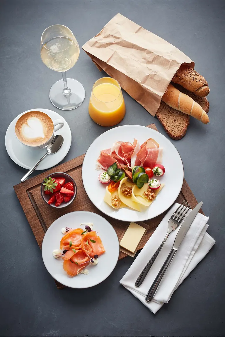 Reichhaltiges Frühstück mit Räucherlachs, Käse, Prosciutto, Brot, Kaffee und Orangensaft