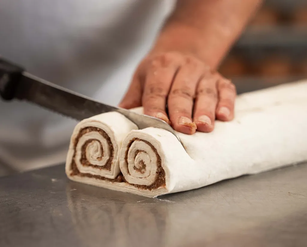 Ein Bäcker beim Schneiden einzelner Nussbrillen von einer großen Teigrolle