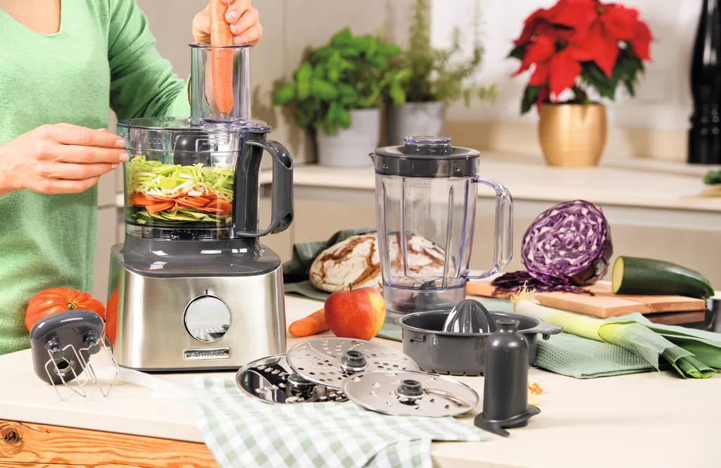 Kenwood Küchenmaschinen auf einer Kücheninsel, umgeben von Zutaten und Zubehör, im Hintergrund Blumen und eine Frau, die eine Küchenmaschine benutzt