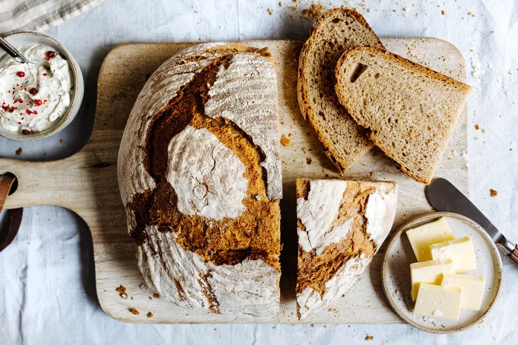 Aufgeschnittenes Brot auf Holzbrett mit Butter, Ansicht von oben