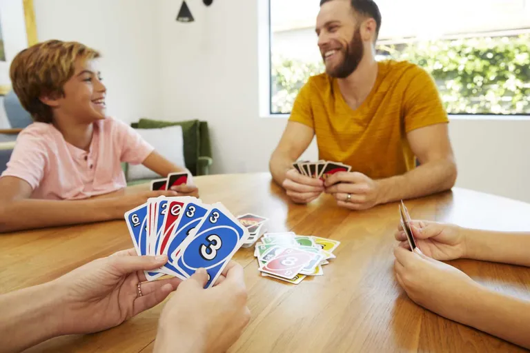 Eine Familie spielt gemeinsam Uno am Esstisch, mit einem Kartenstapel in der mitte und Sonnenlicht vom Fenster