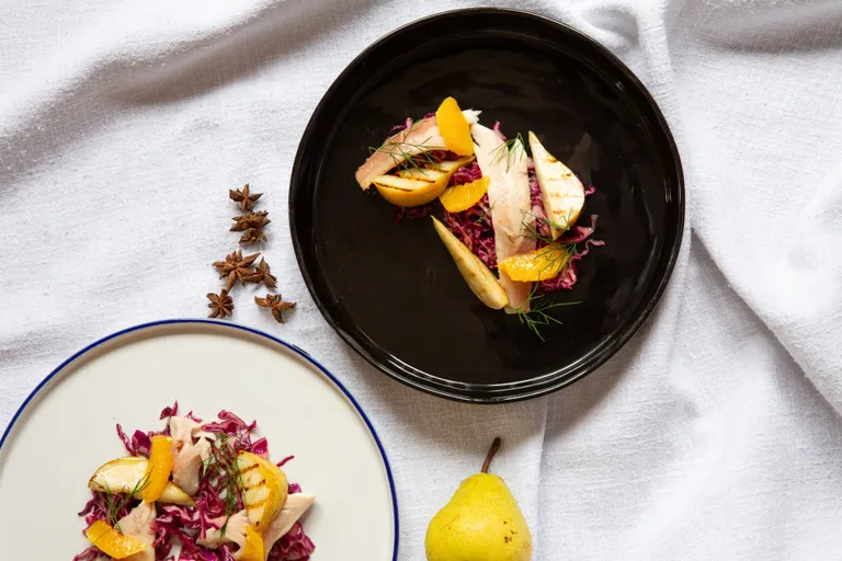 Weihnachtlicher Rotkrautsalat mit Orangenfilets, gegrillter Birne, geräucherter Gebirgsforelle und frischen Kräutern auf zwei Tellern