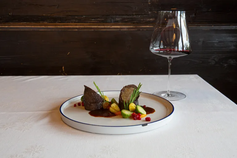Hirschroulade mit Maroni-Semmelknödelfülle, Gemüse und Sauce, serviert mit Rotwein