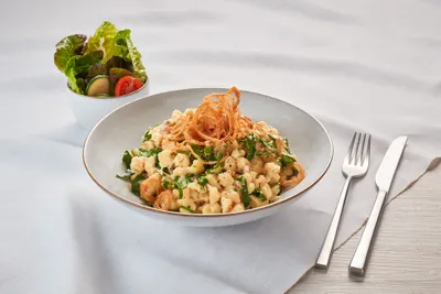 Ein Teller Spätzle mit Bärlauch und knusprigen Zwiebeln, dazu eine kleine Schüssel gemischter Salat, mit Besteck auf einer Tischdecke.