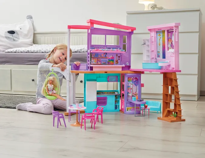 Mädchen spielt mit Barbie Malibu Haus, im Kinderzimmer, im Hitergrund Bett und Kommode