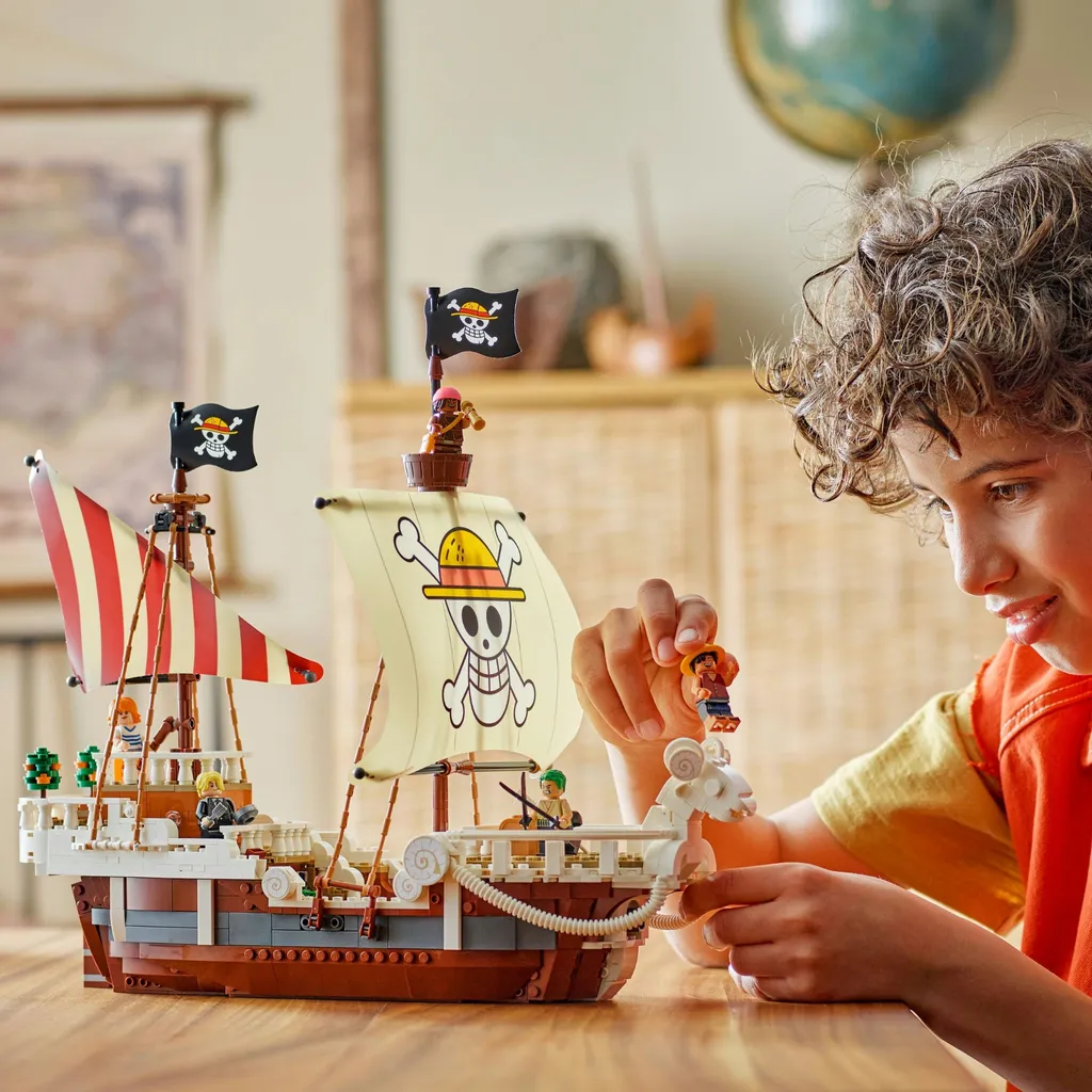 Junge mit lockigen Haaren spielt mit einem Lego-Schiff auf dem Esstisch, mit Figur in der Hand