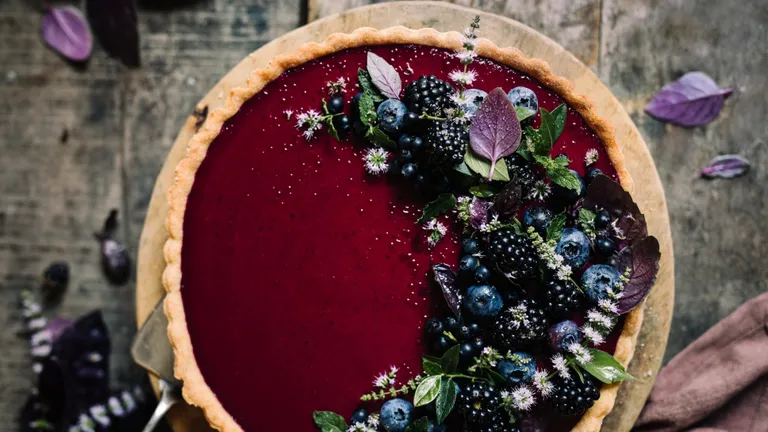 Beerentarte mit Dekoration aus Beeren, Kräutern und Blüten auf einem dunklen Holzhintergrund