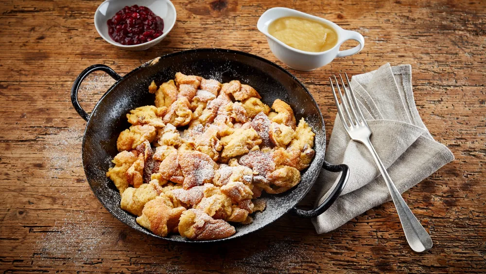 Kaiserschmarren mit Apfelmus in einer schwarzen Pfanne auf rustikalem Holztisch