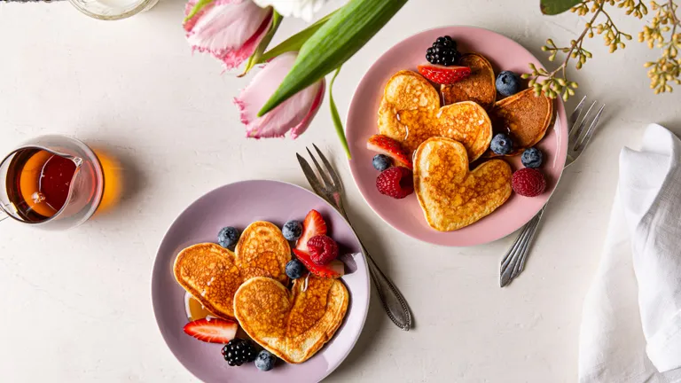 herzförmige Pancakes mit Beeren auf einem hellen Tisch mit einer Tulpenvase
