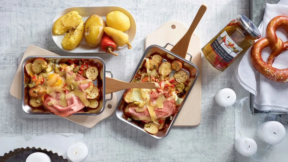 Brezeln mit Ei und Leberkäse in kleinen Pfännchen auf einem weißen TIsch