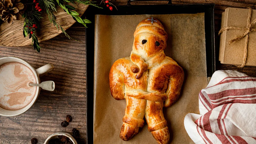 Festliches Brot in Form einer Figur auf einem Backblech, daneben Kakao, ein Holztablett und eine Geschenkbox.