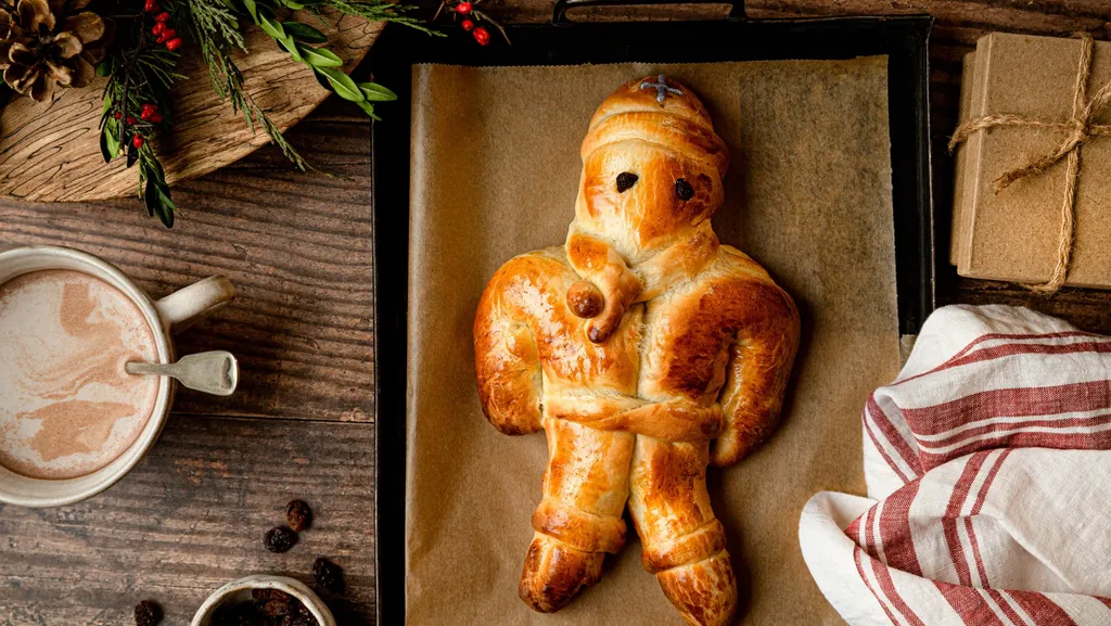 Festliches Brot in Form einer Figur auf einem Backblech, daneben Kakao, ein Holztablett und eine Geschenkbox.