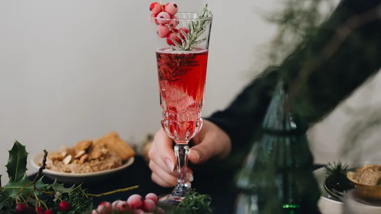 Eine Hand hält ein Glas Cranberry Bellini vor festlichem Hintergrund