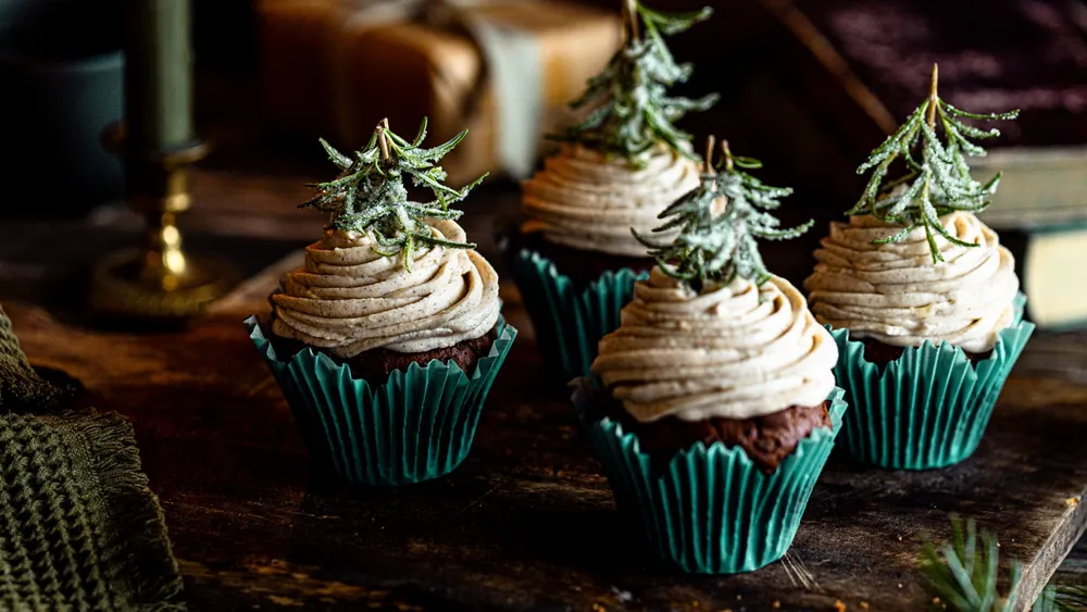 Cupcackes mit Cremehaube und einem Rosmarinzweig, wer wirkt wie ein Tannenbaum, auf dunklem HIntergrund.