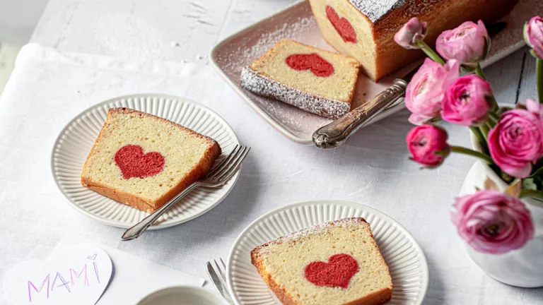 Kastenkuchen mit eingearbeitetem, roten Herz, aufgeshnitten und auf Tellern angerichtet, daneben Ranunkeln