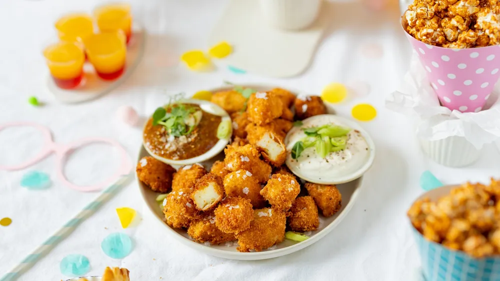 Knusprige Haloumi Bites mit 2 Dips in einer weißen Porzellanschüssel auf einer bunt dekorierten, weißen Tischdecke