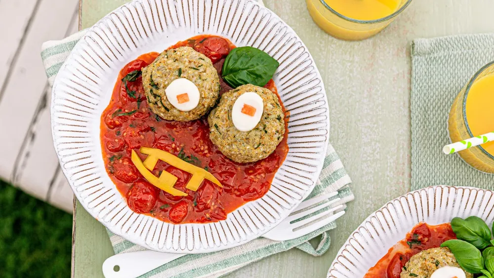 Zwei Gemüse-Bratlinge mit Eiern und roter Paprika auf Tomatensoße, garniert mit Basilikum, auf einem Pappteller.