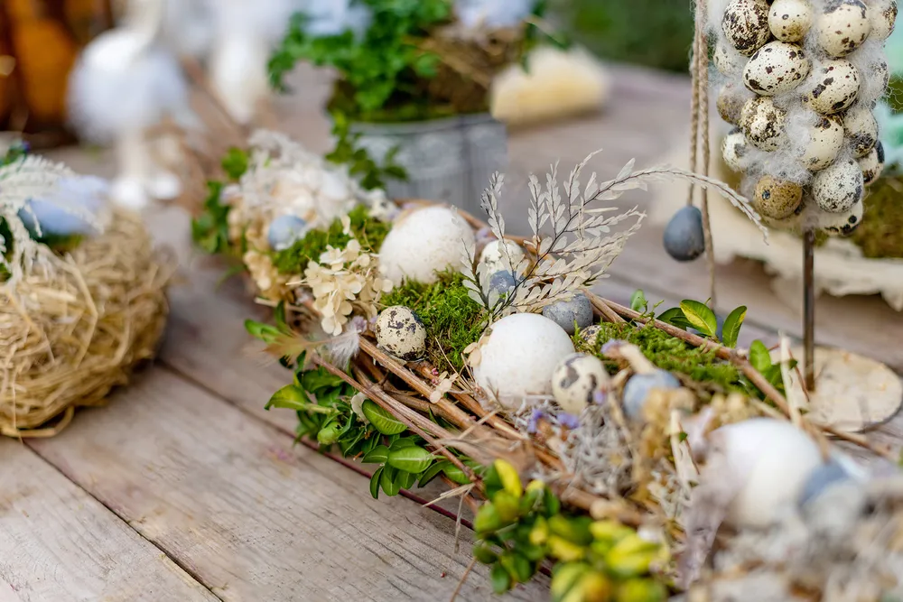 Tischdekoration zum Thema Eier mit Wachteleiern, Moos und Trockenblumen auf einem rustikalen Holztisch.