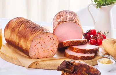 Drei Scheiben Leberkäse auf einem Holzbrett, dazu Kirschtomaten, Brot, Senf und im Hintergrund ein Keramikkrug.