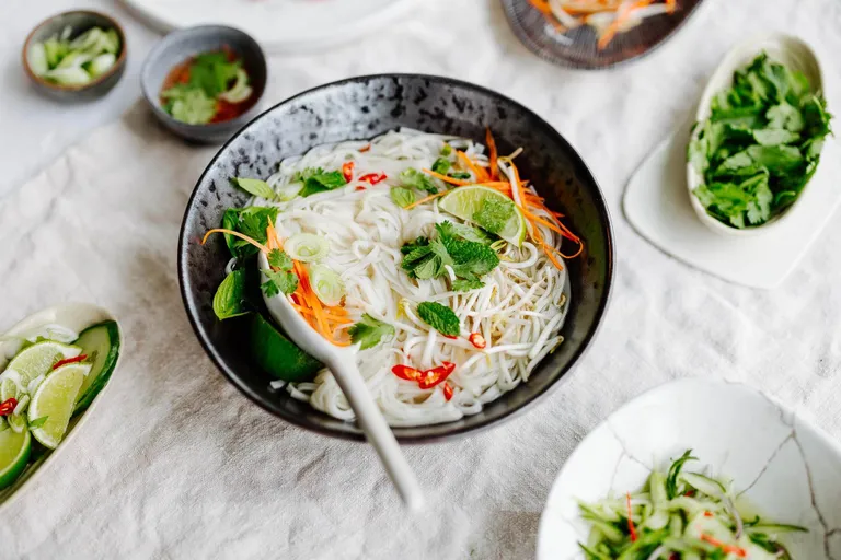 Vietnamesische Pho mit Reisnudeln, frischen Kräutern, Limette und Gemüse